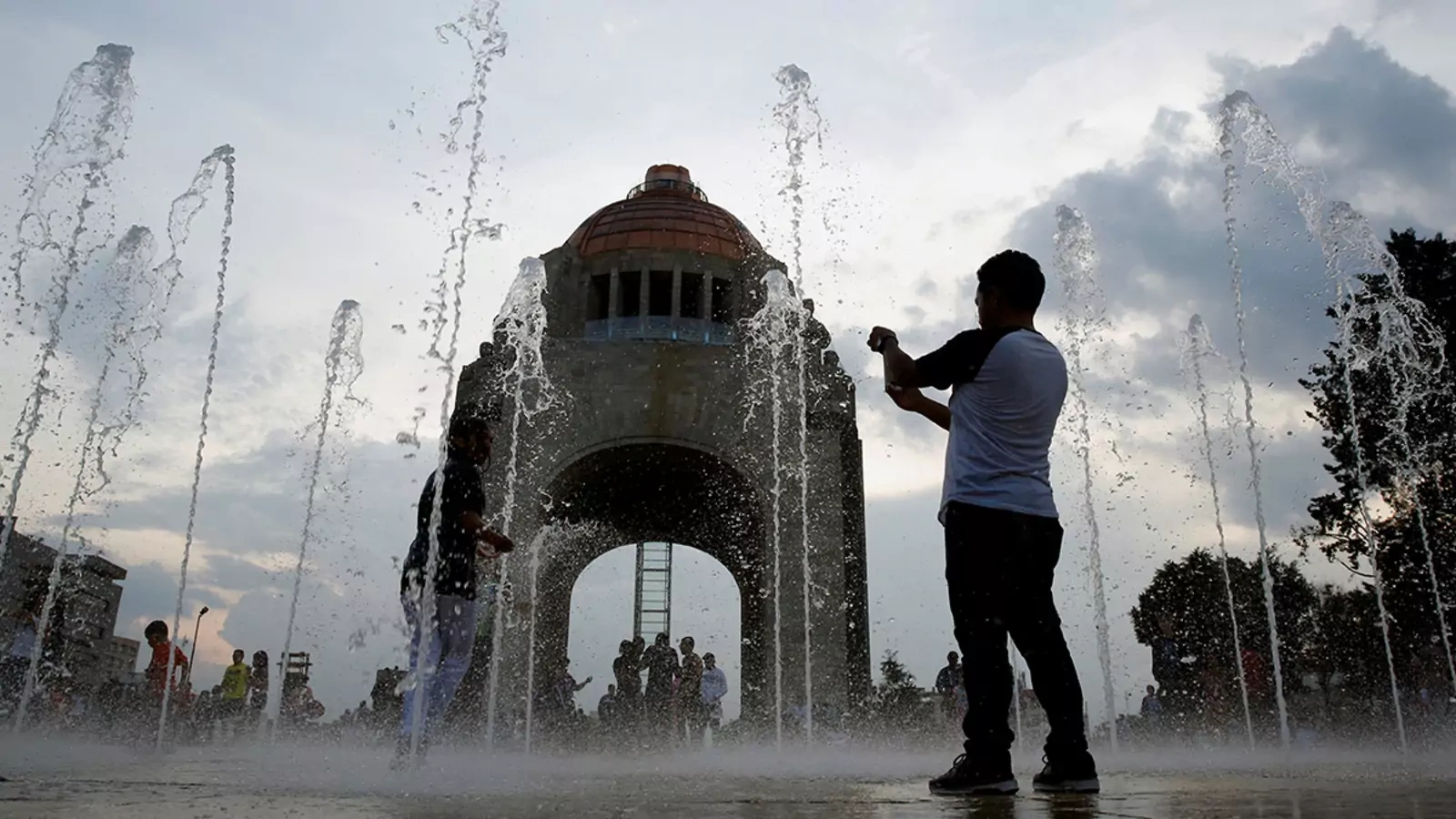 A man takes a picture by a fountain at the Monument of the Revolution in Mexico City.