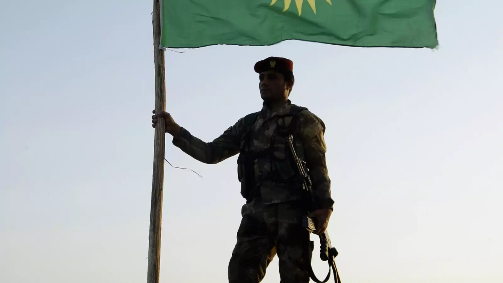 A Kurdish Peshmerga soldier holds a Kurdistan flag during a deployment in the area near the northern Iraqi border with Syria