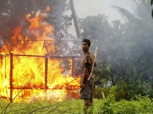 An ethnic Rakhine man holds homemade weapons as he stands in front of a house that was burnt during  fighting between Buddhist Rakhine and Muslim Rohingya communities in Sittwe.