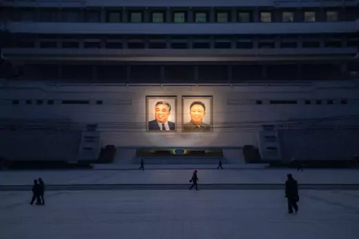 Pedestrians walk past portraits of Kim Il-sung and Kim Jong-il.