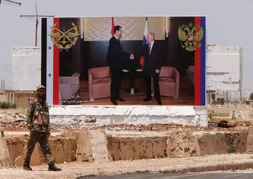 Syrian soldier in front of poster of Bashar al Assad