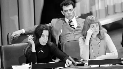 A women speaks at a committee meeting while a man and woman look on next to her.