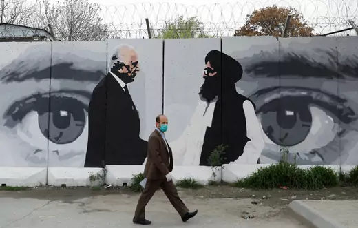 An Afghan man wearing a protective face mask walks past a wall painted with photo of Zalmay Khalilzad, U.S. envoy for peace in Afghanistan, and Mullah Abdul Ghani Baradar, the leader of the Taliban delegation, in Kabul, Afghanistan.