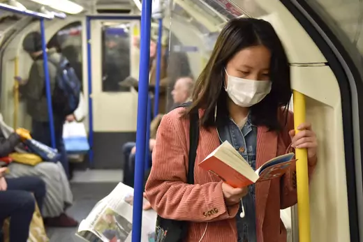 A woman holds on to the handrail as she reads a book while wearing a face mask on the Picadilly Line tube train on March 02, 2020 in London, England.