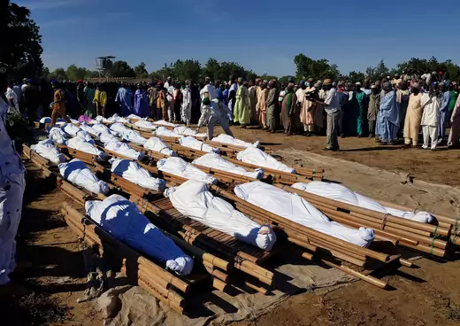 Men gather near dead bodies of people who were killed by militant attack, during a mass burial at Zabarmari, in the Jere local government area of Borno State. The bodies are covered in white cloth and placed on wooden structures used to carry the bodies.