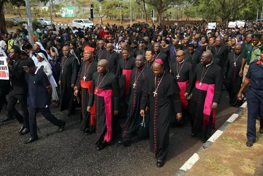 A procession of Nigerian Catholic bishops and faithfuls wearing black, religious dress walk on a street to protest killings of Nigerians.