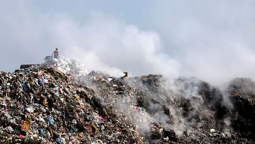 Smoke rises from a landfill full of waste.
