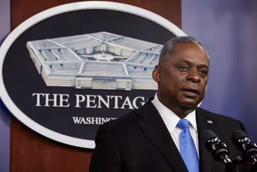 U.S. Defense Secretary Lloyd Austin speaking into a microphone. Behind him is a sign with an image of the Pentagon.