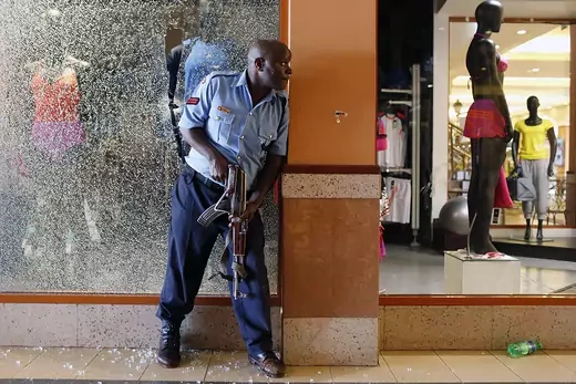 A police officer with machine gun hides behind wall in the Westgate Shopping Center, looking for suspects.
