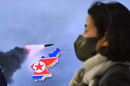 A woman walks past a television report showing a news broadcast with file footage of a North Korean missile test, at a railway station in Seoul on March 24, 2022.
