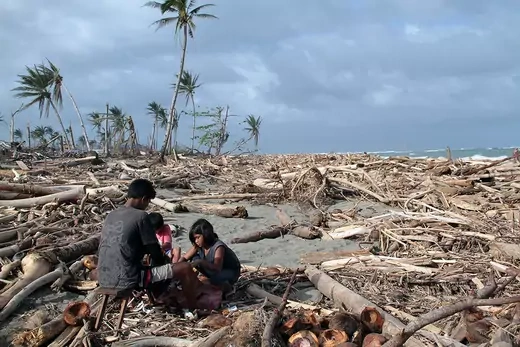 Photo showing a father with his two children sitting in rubble on a beach in the Philippines after a typhoon. 