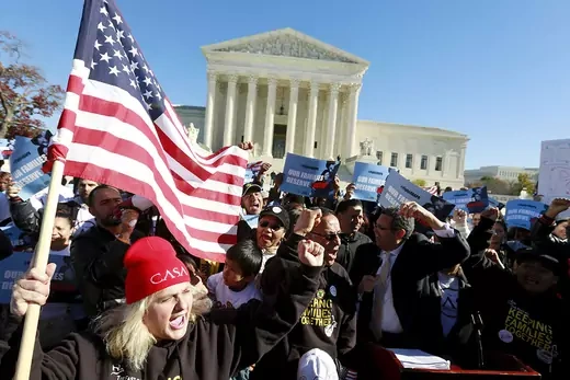 People, some carrying a U.S. flag and others signs, rally in front of the U.S. Supreme Court to mark the one-year anniversary of President Barack Obama's executive orders on immigration 