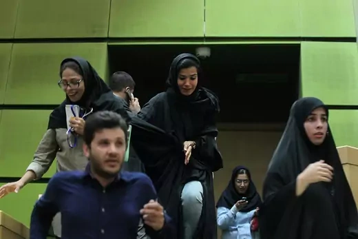 Female and male staff exit Iran's parliament building in distress.