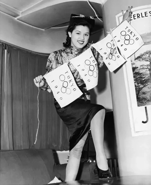 A woman holds flags showing the Olympic rings and reading Tokyo 1940.