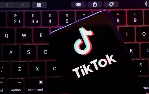 This image shows a keyboard with a phone on the top. The phone screen displays the logo for the popular app TikTok.