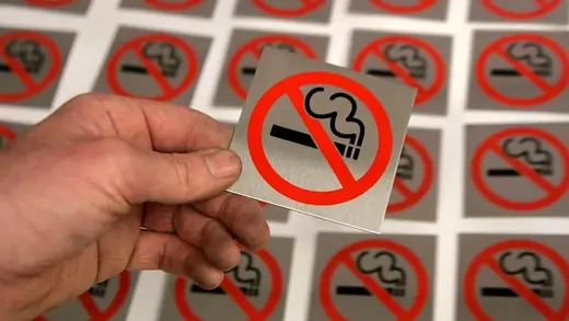 Hand holds up smoking prohibited placard.