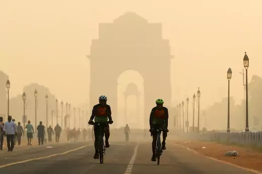 Men ride their bicycles along Kartavya Path in front of the smog-shrouded India Gate in New Delhi.