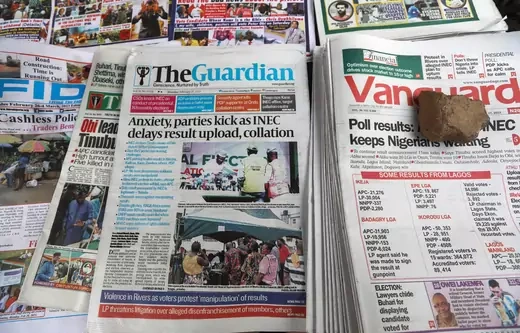 A pile of newspapers in Nigeria with various topics related to the recent elections are shown.