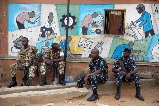 Nigerian police officers sit in front of a colorful mural. 
