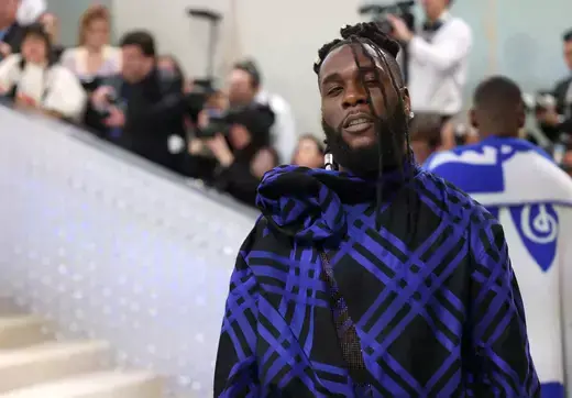 Nigerian singer Burna Boy is shown wearing a black and purple cloak while posing at the annual Met Gala in New York City. 