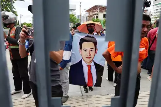 A picture of Thai prime ministerial candidate is held up as protestors stand behind an iron fence.