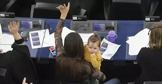 Female legislator raises hand to participate while holding child.