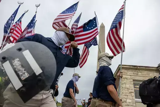 Masked members of the far-right group Patriot Front march through Washington, DC, holding American flags and riot shields.