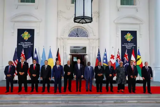 Pacific Island leaders and U.S. President Joe Biden stand outside the White House on a red carpet with national flags behind them.