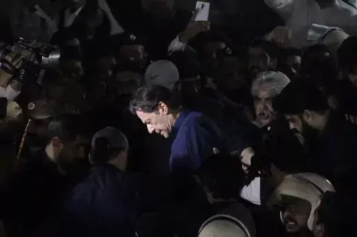 Former Prime Minister Khan wears a blue suit while surrounded by people in black.