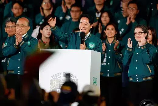 Taiwan's president-elect speaks in front of a white podium wearing an emerald green jacket as members of his party stand behind him clapping.
