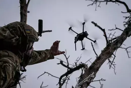A man in camo releases a drone into the sky.