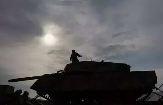 A silhouette of a large tank is shown outside with a man in uniform sitting on top. 