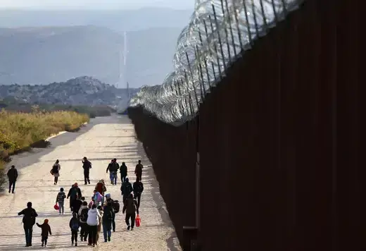 Asylum-seeking migrants walk toward a makeshift camp to await processing by the U.S. Border Patrol after entering the United States on December 1, 2023, in Jacumba Hot Springs, California.