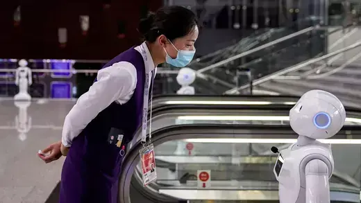 A woman wearing a face mask looks at a robot.