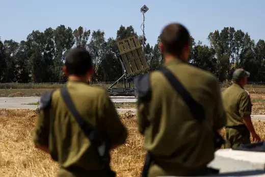 Two men as viewed standing in front of an Iron Dome anti-missile battery.
