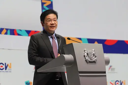 Singapore's deputy prime minister stands at a silver podium wearing a black suit and maroon tie.