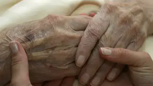 A young carer holds the hands of an elderly woman. 