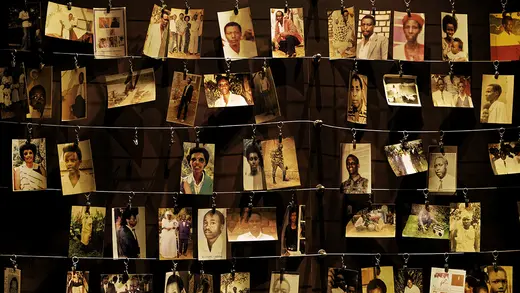 Several photographs of people that were lost in the genocide hang on hooks from wires in five rows.