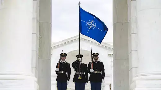 A color guard from the 3d U.S. Infantry Regiment (The Old Guard) carries the NATO flag at the Arlington National Cemetery, Arlington, Virginia and two other soldiers stand on either side.