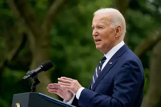 Biden as viewed standing at a podium in a navy suit. 