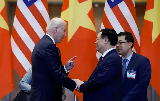 President Biden shakes hands with the former leader of Parliament in Vietnam in front of American and Vietnamese flags.
