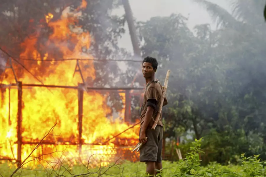 An ethnic Rakhine man holds homemade weapons as he stands in front of a house that was burnt during fighting between Buddhist Rakhine and Muslim Rohingya communities in Sittwe.