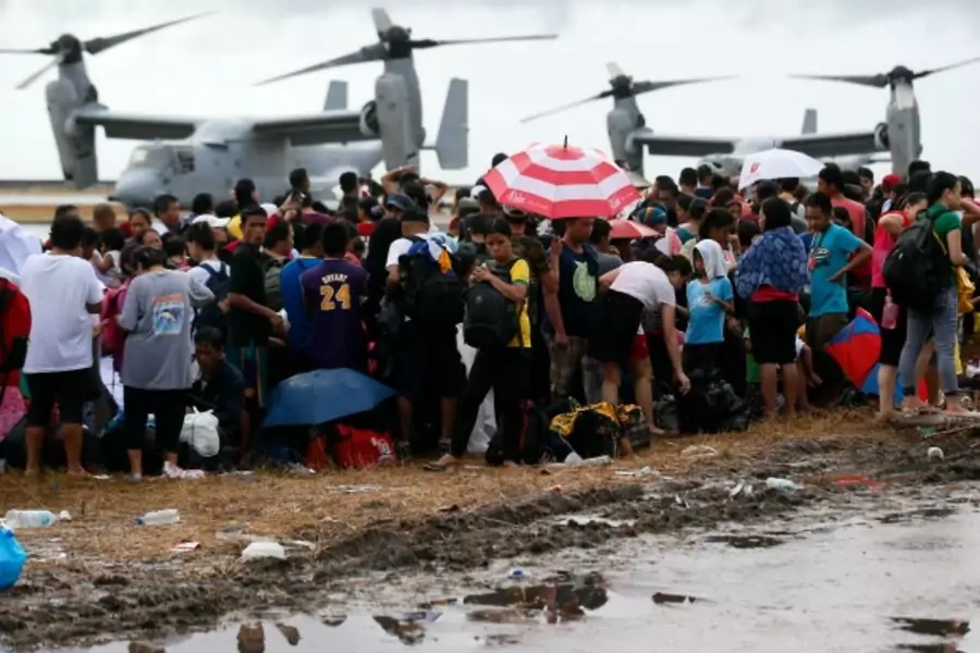 People wait to be airlifted to Manila as Ospreys from the U.S. Navy Ship (USNS) Charles Drew taxi on the tarmac in the background, at Tacloban airport on November 14, 2013 (Wolfgang Rattay/Courtesy Reuters).