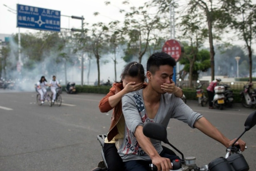 Residents cover their faces as they ride a motorcycle along a street after tear gas was released by police to disperse a protest against a chemical plant project in Maoming, Guandong province, China on March 31, 2014. (Stringer/Courtesy Reuters)