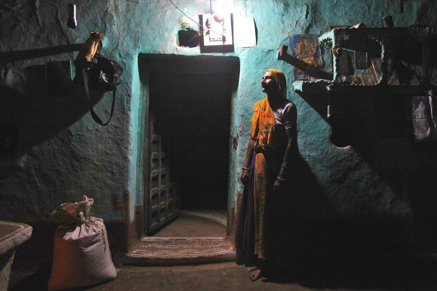 Sampat Bai stands inside her house illuminated by a compact fluorescent lamp powered by solar energy, in the central Indian state of Madhya Pradesh.