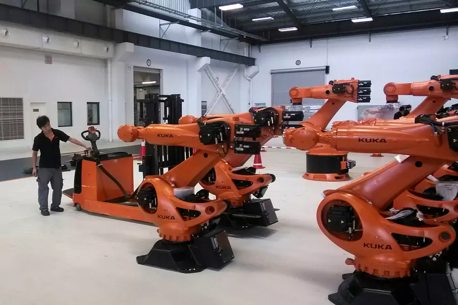 A staff member stands next to robots at a plant of Kuka Robotics in Shanghai, China