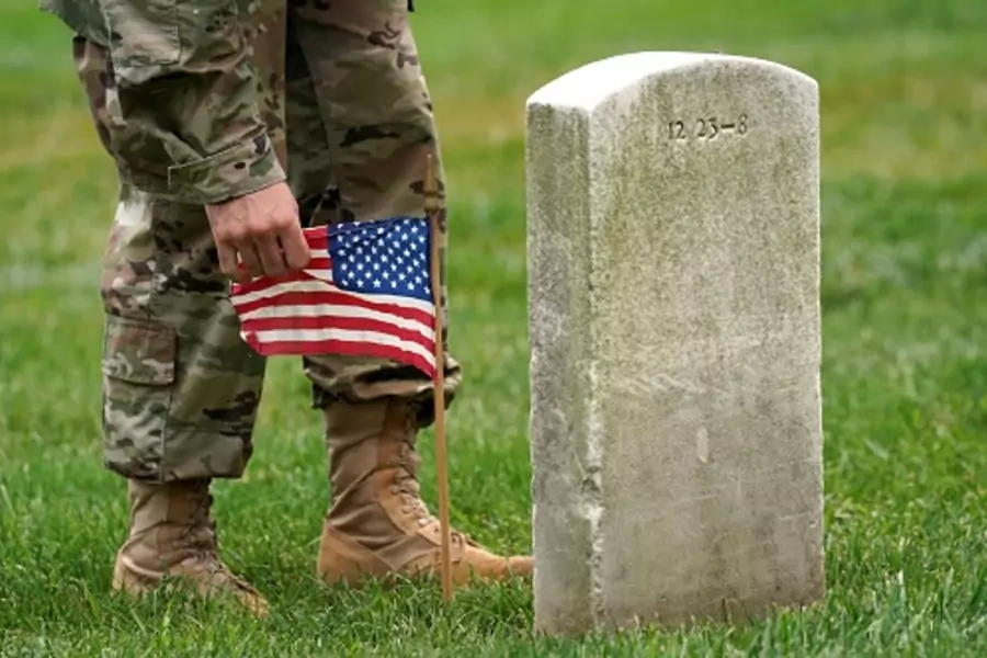A soldier from the 3rd U.S. Infantry Regiment places a flag at a headstone at Arlington National Cemetery. 