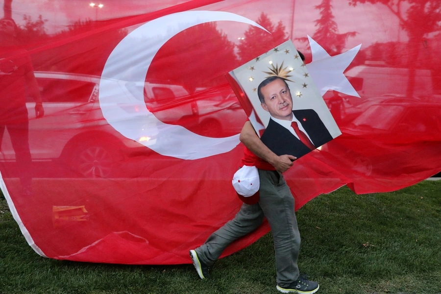 A supporters of Turkish President Tayyip Erdogan holds his picture in front of a Turkish flag, in front of Turkey's ruling AK Party (AKP) headquarters in Istanbul, Turkey. June 24, 2018.