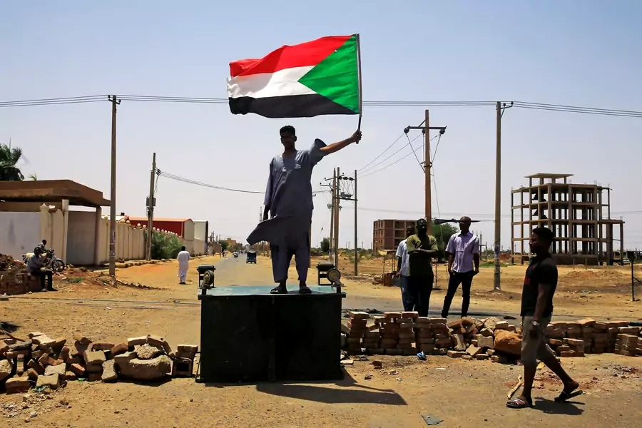 A Sudanese protester holds a national flag as he stands on a barricade along a street, demanding that the country's Transitional Military Council hand over power to civilians, in Khartoum, Sudan, on June 5, 2019. 