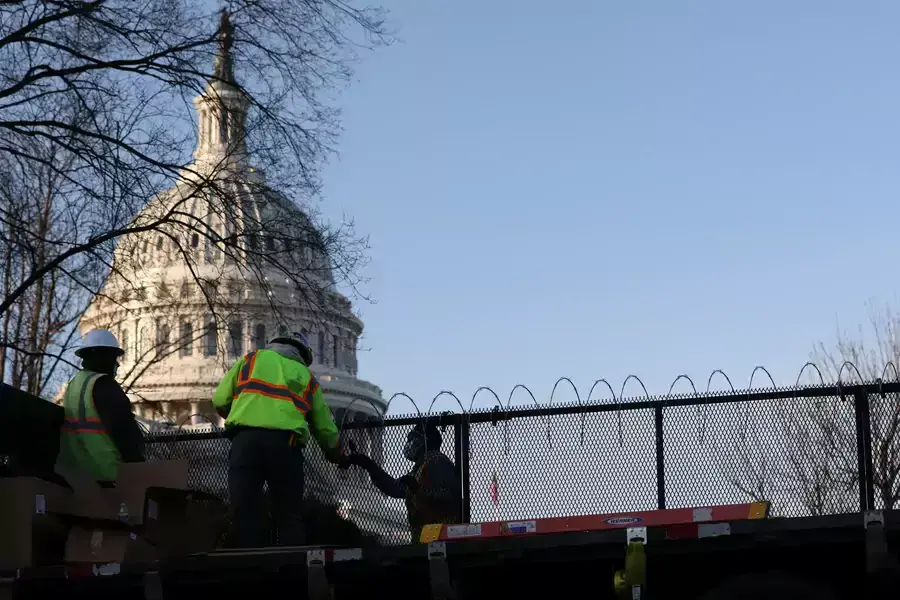 Workers install razor wire atop the fence surrounding the U.S. Capitol in the wake of the January 6th assault on the Capitol